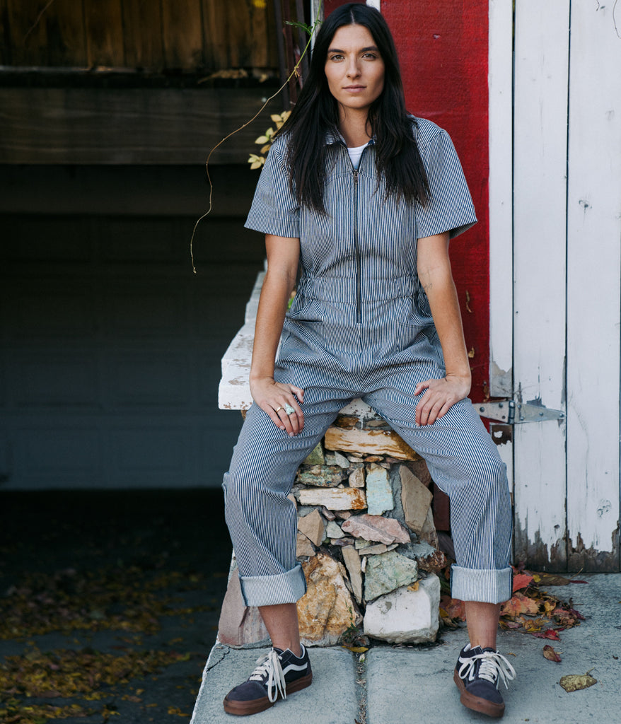 A woman wearing Bodie Women's Coverall in indigo railroad color by Deso Supply Co. 1