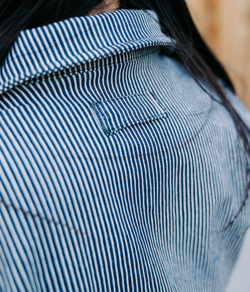  A close-up of a woman wearing the Bodie Women's Coverall in indigo railroad color from the back view.