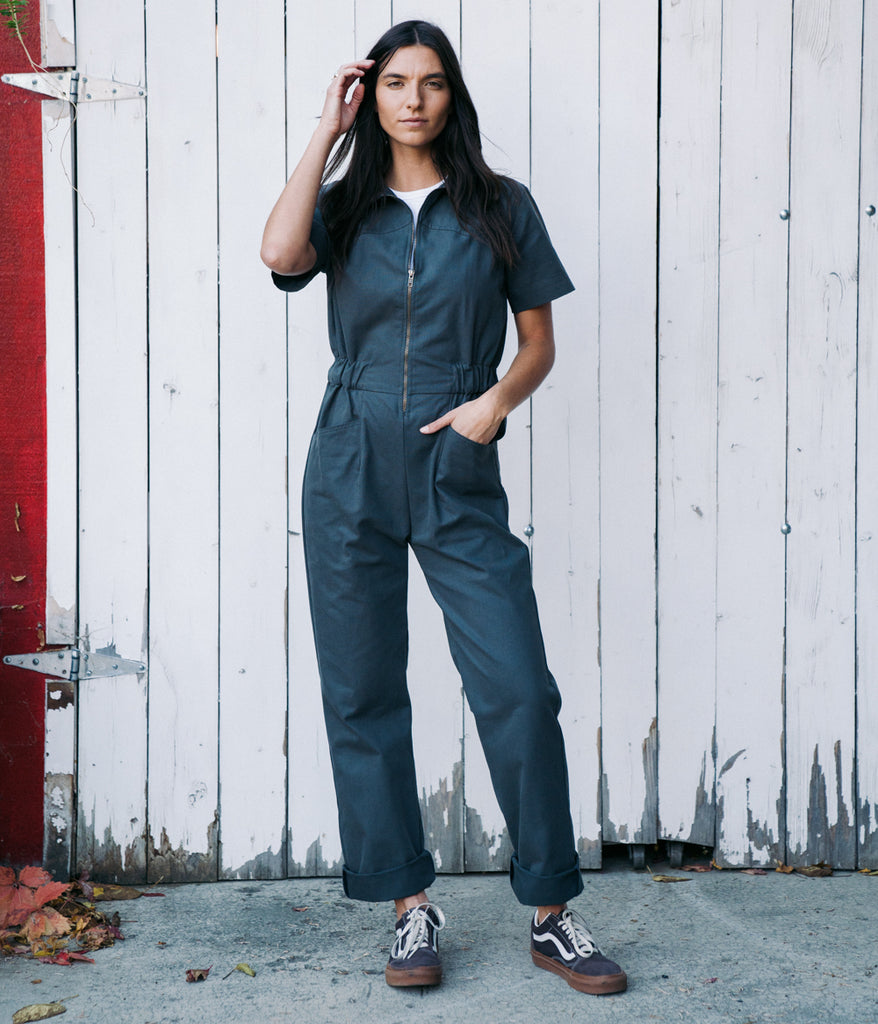 A woman wearing a bodie coverall in graphite color by Deso Supply Co.