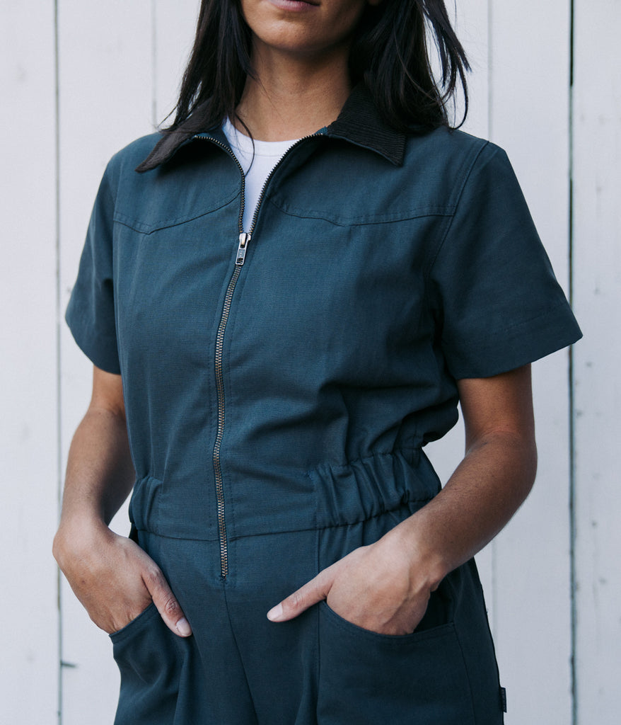 A woman wearing a bodie coverall in graphite color by Deso Supply Co. 1