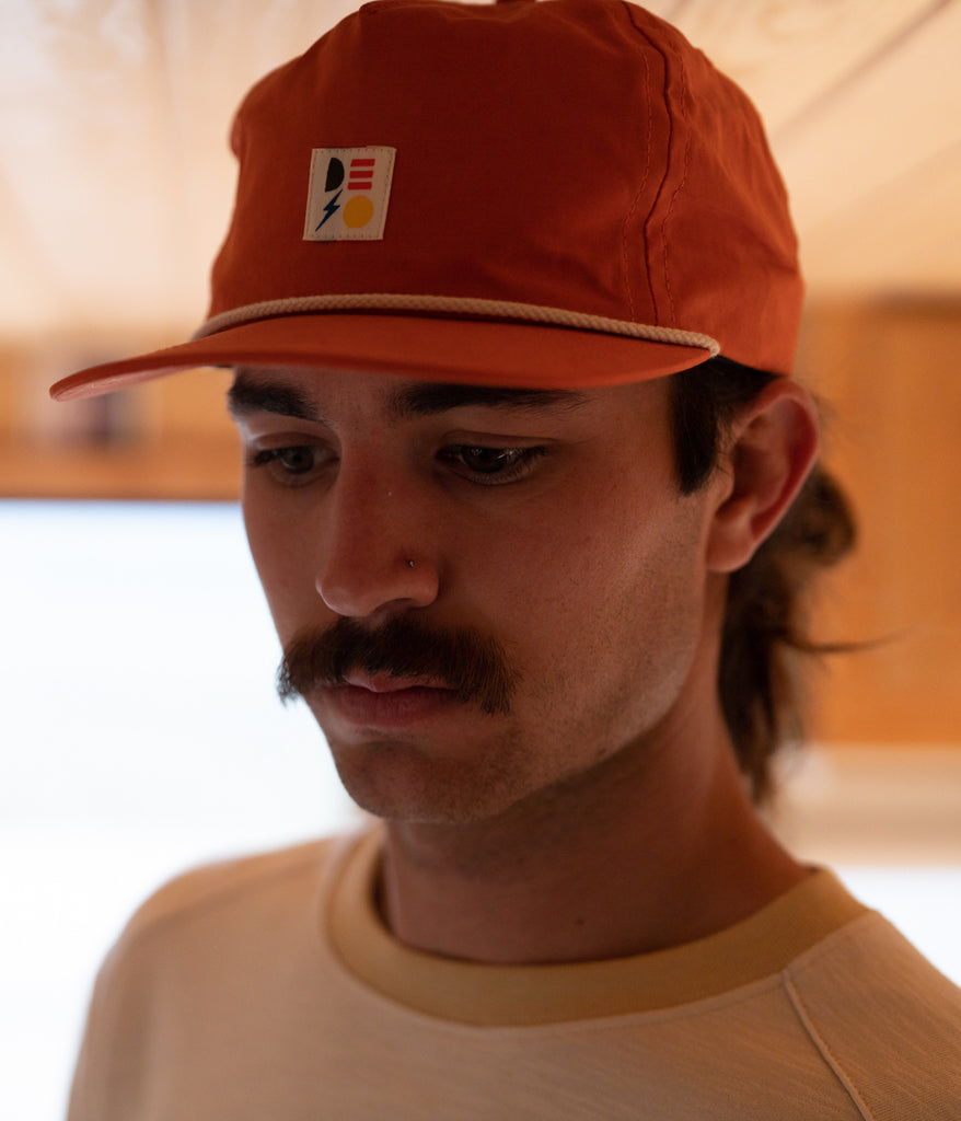 A man wearing Shapes 5-panel cap in brick color by Deso Supply Co. 1
