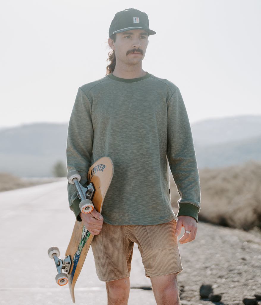  A man with a skateboard wearing the Primary Slub long sleeve in sage color by Deso Supply Co.