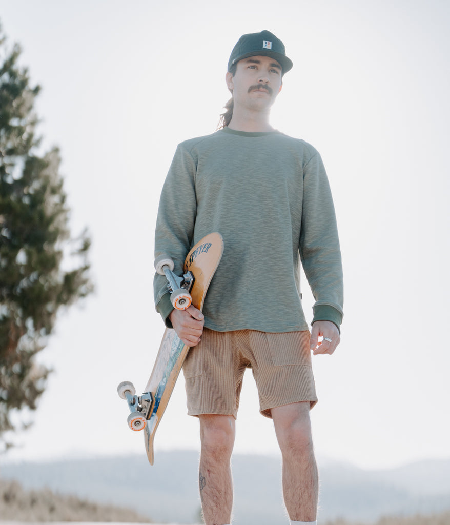 A man with a skateboard wearing the Primary Slub long sleeve in sage color by Deso Supply Co. 1