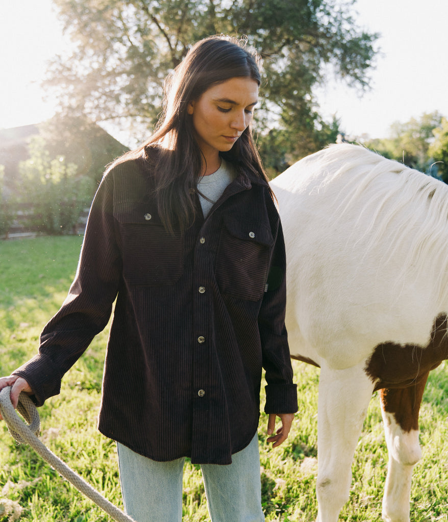 A woman standing next to a horse wearing a Valhalla Cord Shirt