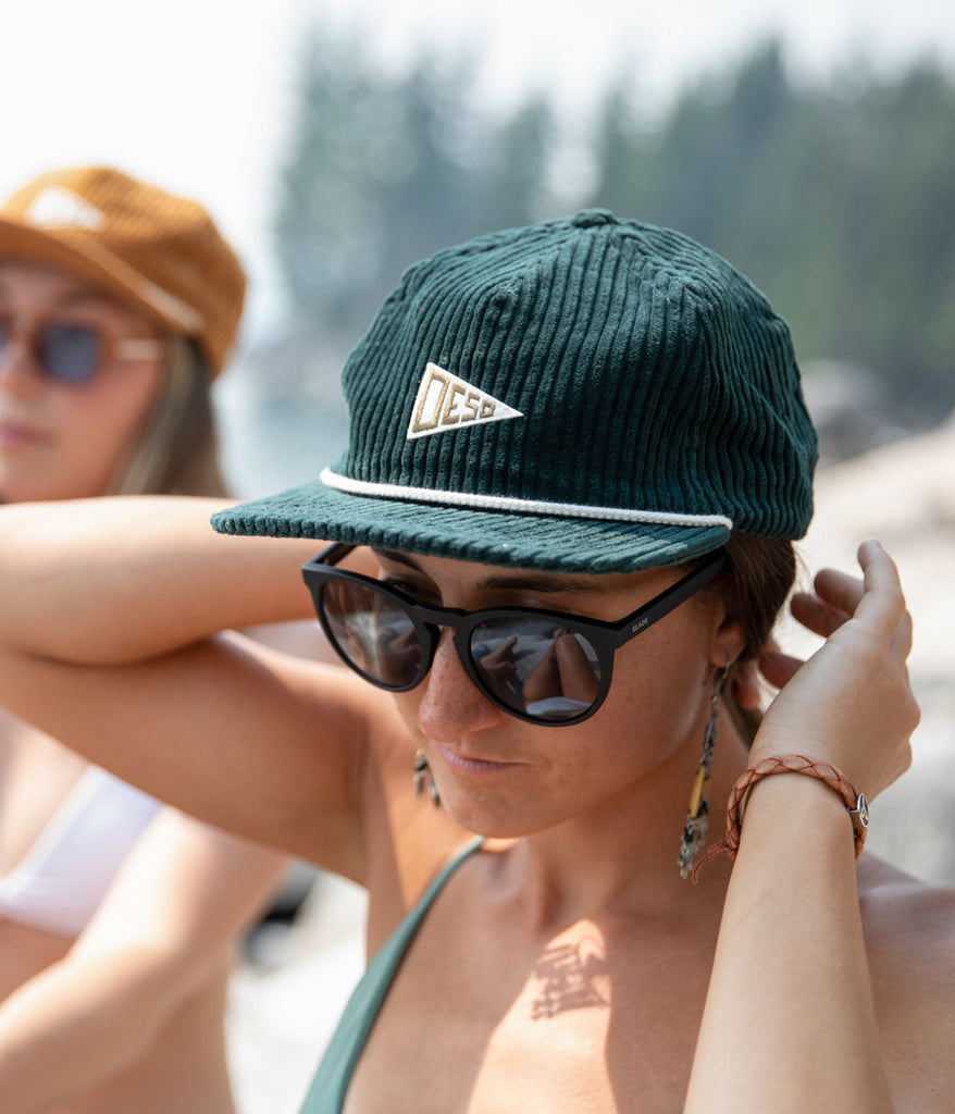 A woman wearing the Lola 5 Panel Cap in forest color by Deso Supply Co.