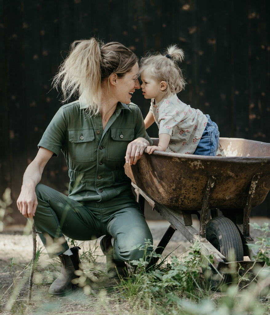 A woman next to a child dressed in dark sage-colored Homewood Coveralls by Deso Supply Co.