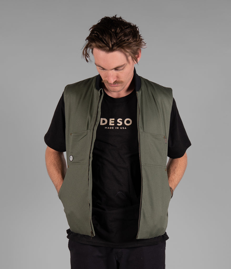 A man wearing a Hard Chore Vest in dark sage color by Deso Supply Co.