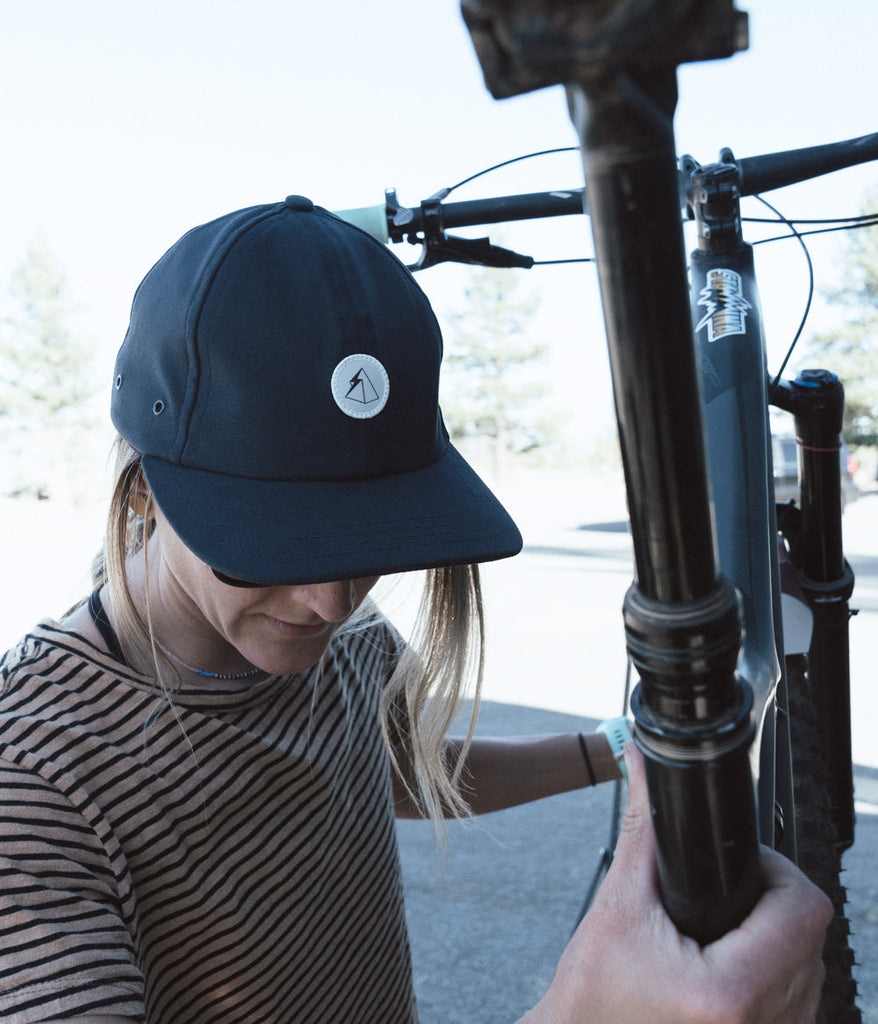 A woman with a bicycle wearing Hatchet 6 Panel Cap in midnight blue by Deso Supply Co.